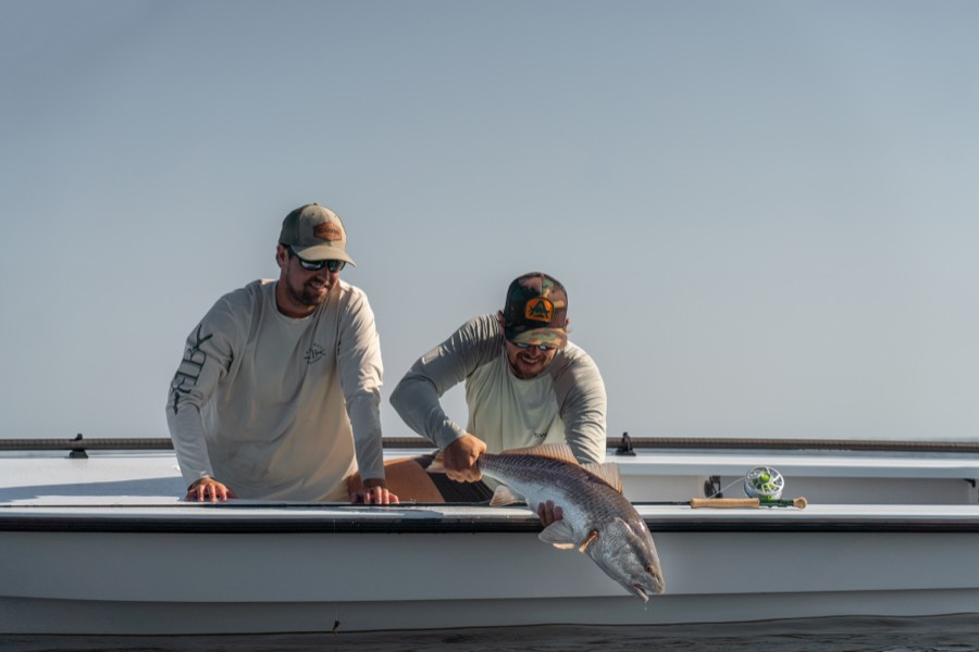 Two anglers on the skiff lifting a redfish beside a fly rod